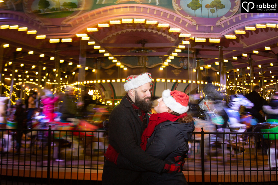 Engagement photo in front of a carousel with the carousel in motion and the couple staying still in front of it at Canada's Wonderland Winterfest.