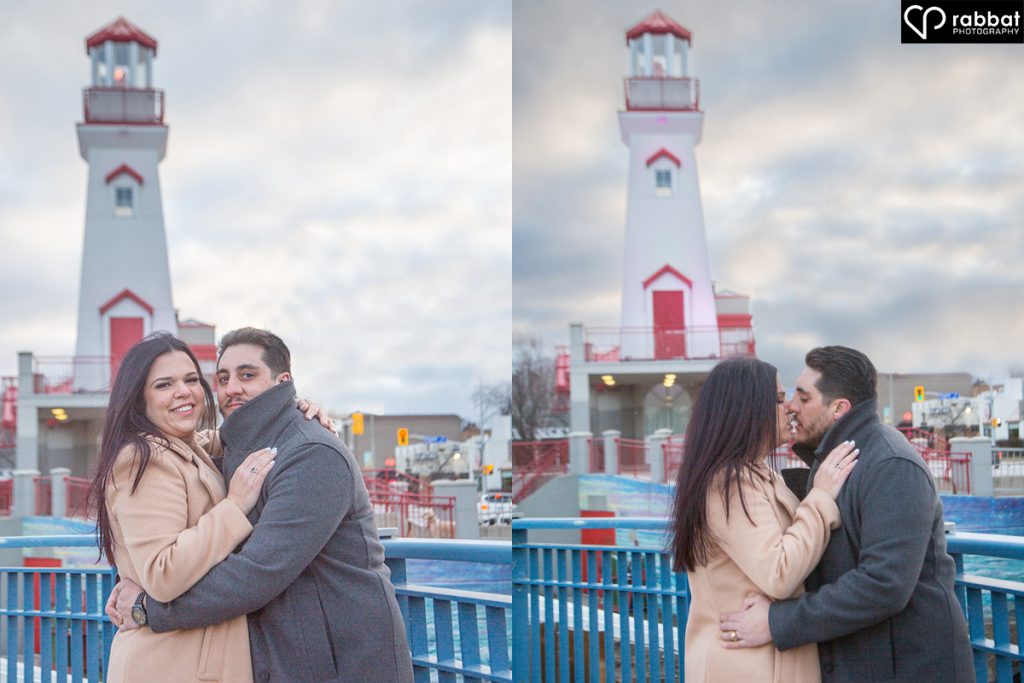 Woman on left and man on right wearing winter coats in front of the white lighthouse in Port Credit with a red door and red roof. Two side by side vertical photos. They are looking at the camera in the photo on the left and kissing in the photo on the right.
