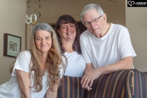 Indoor portrait of an 80 year old white man with his two grown daughters.