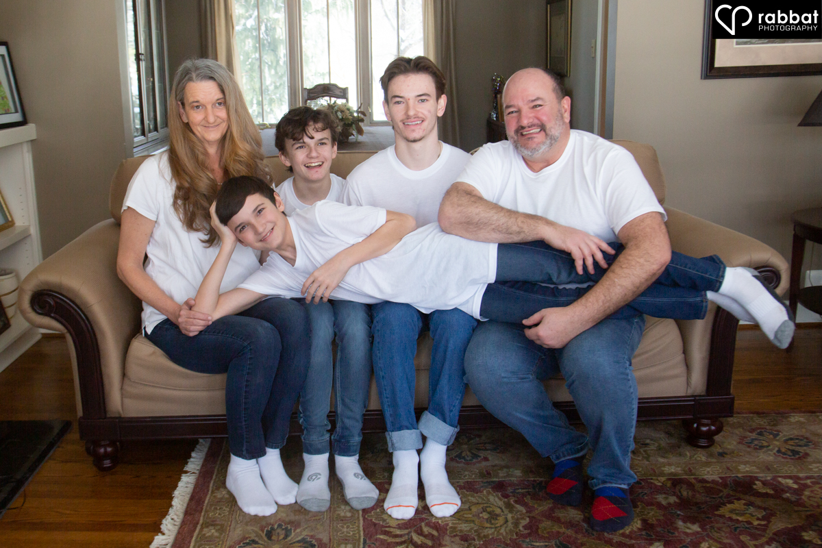 Family of five on couch, all wearing white t-shirts. The kids are all boys and the youngest is around 13 and is lying on the laps of everyone else.