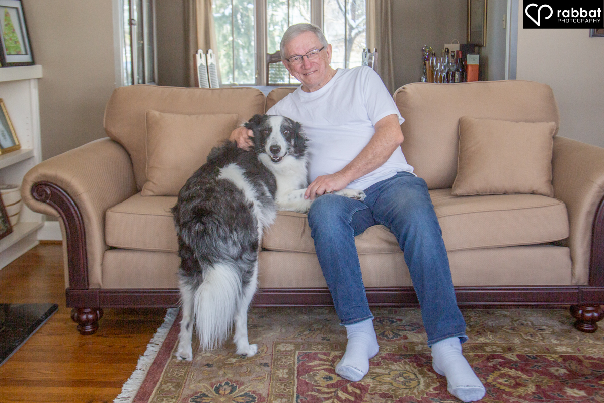 Man on couch with his dog, who is standing but has his right paw on the man's lap.