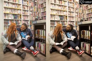 Two side by side vertical photos of a couple sitting on floor in front of bookshelves filled with comics and anime. They are each holding a comic book. The books are open and they are looking at each other in both photos. Man is black and woman is Metis with a light complexion and red hair.