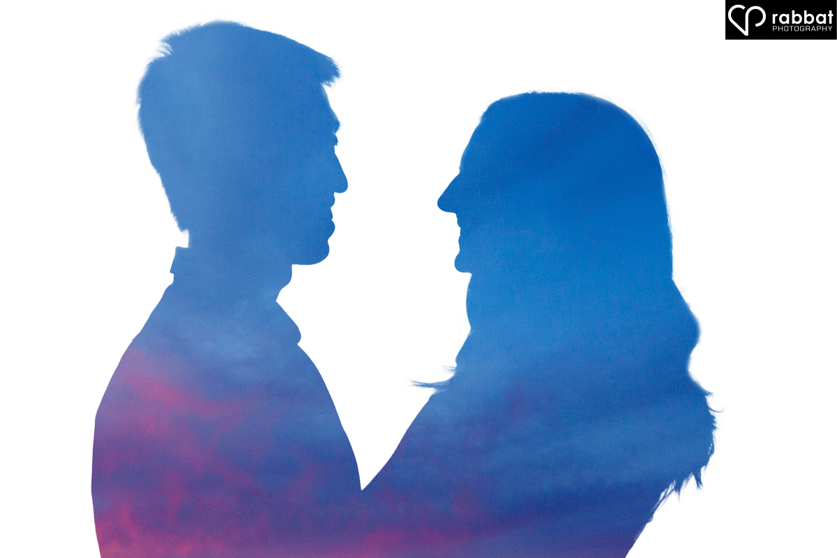 Sunset silhouette of couple looking at each other. The background is totally white and the sunset is inside their silhouettes. Their heads are blue and their bodies are pinkish.