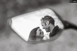 Black and white image of a happily engaged couple reflected in a motorcyle mirror