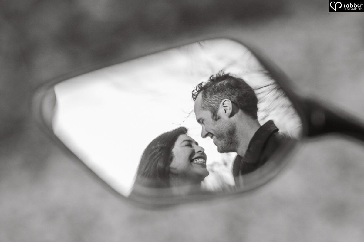 Black and white image of a happy couple reflected in a motorcyle mirror