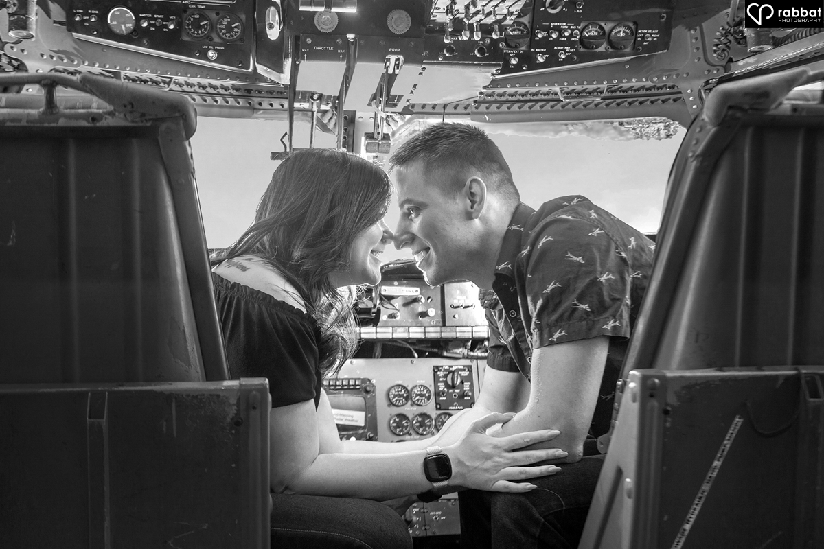 Black and white photo of a couple touching heads and smiling at each other in an airplane cockpit.