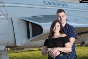 Man hugging woman from behind in front of a Canadian Forces airplane.