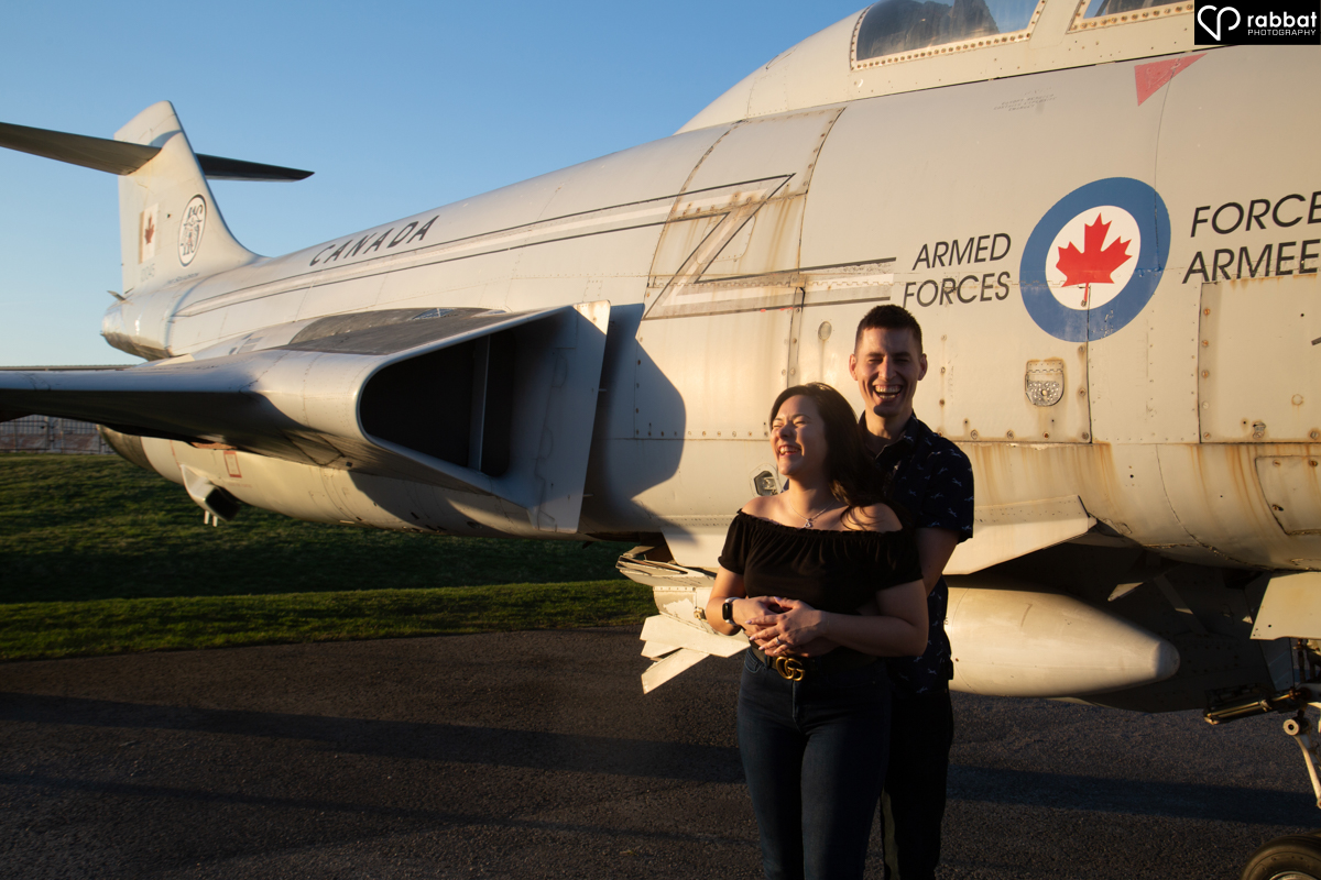 Man hugging woman from behind in front of gray Canadian Forces airplane