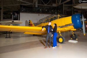 Man and woman dressed in blue and black in front of yellow RCAF airplane.