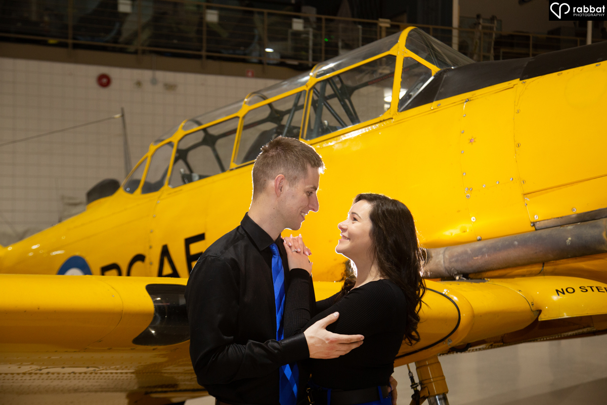 Close-up photo of couple dressed in blue and black in front of RCAF airplane.