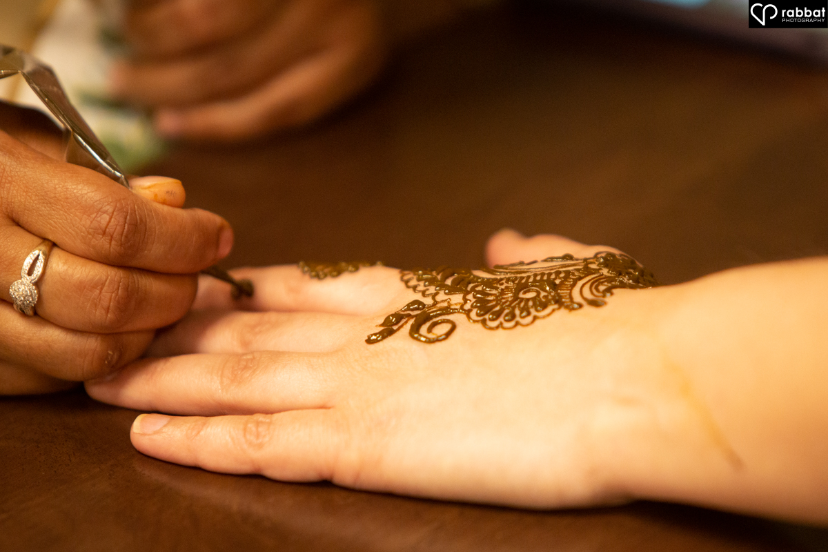 Photo of a hand, a hand holding henna brush and decorative henna on a woman's hand.