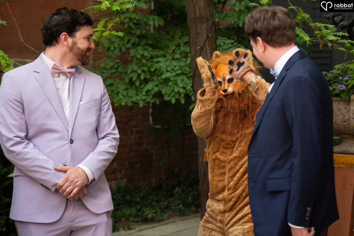 Person dressed up as a lion sneaking up behind shocked groom and best man.
