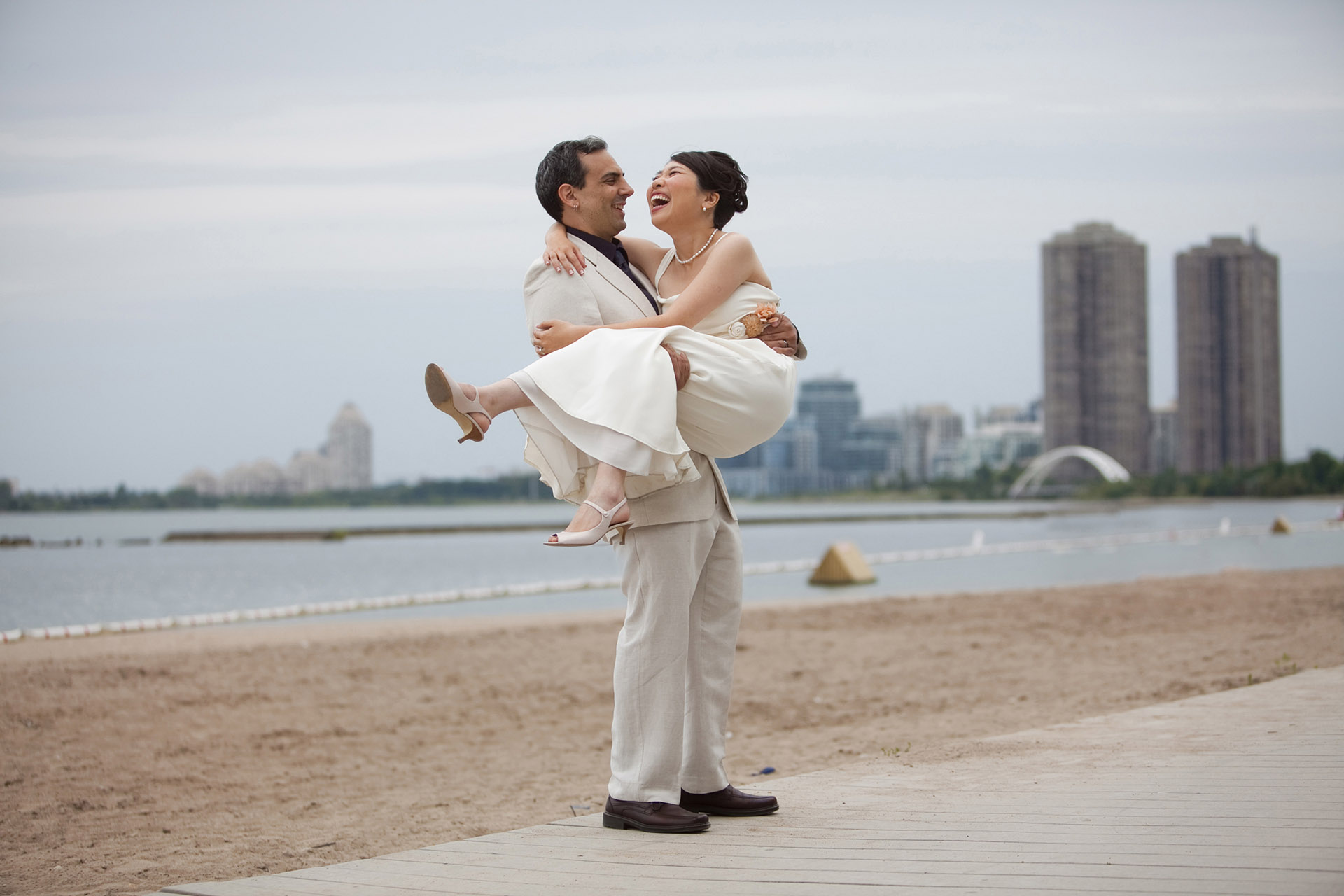 Groom lifting and laughing with bride during a candid beach wedding portrait session, captured by an unscripted Toronto wedding photographer.
